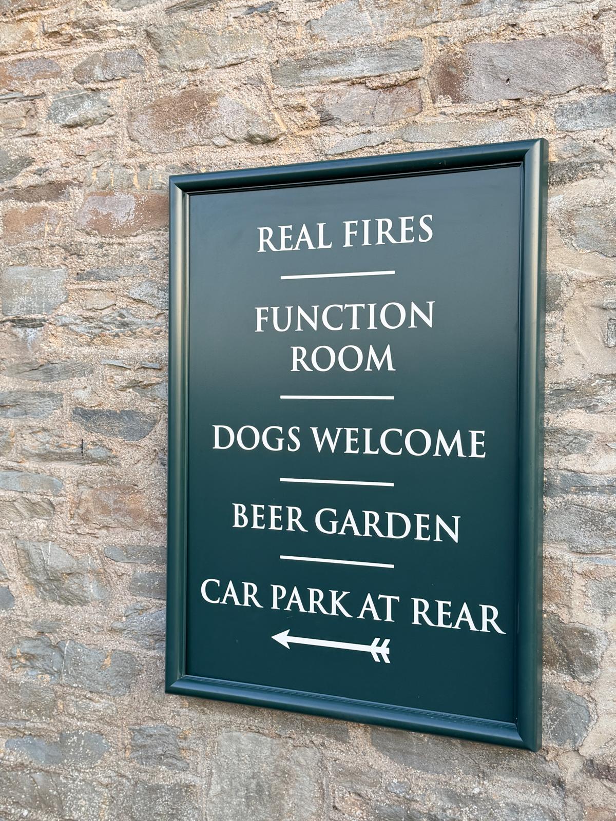 Painted sign at the pub listing real fires, function room, dogs welcome and beer garden